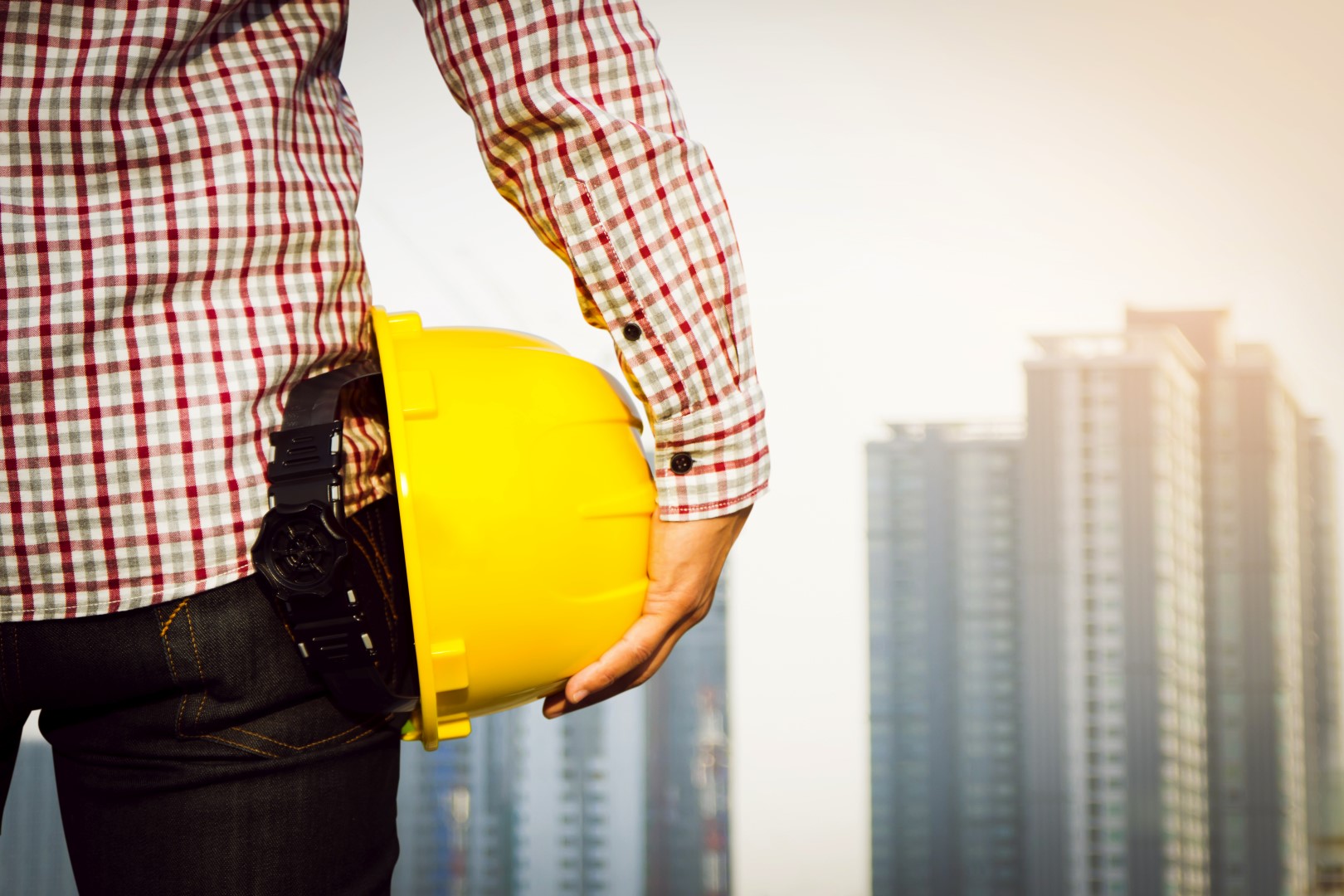 Hand's engineer worker holding yellow safety helmet with building on site background.