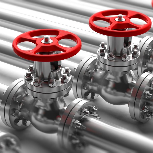 Some pipes on the ground with red valves on top of the pipes.