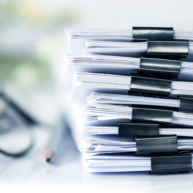 Some objects are zoomed in on a table, to the left is a pile of documents. In the centre is a pencil. On the far left is a pair of glasses.