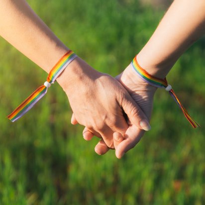 Two people are holding hands while wearing LGBTQIA+ pride bracelets Two people are holding hands while wearing LGBTQIA+ pride bracelets