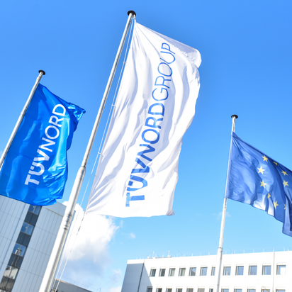 TÜV NORD and EU flags wave outside modern office buildings under a clear blue sky.