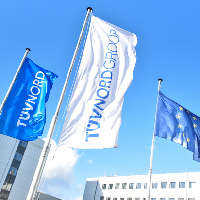TÜV NORD and EU flags wave outside modern office buildings under a clear blue sky.