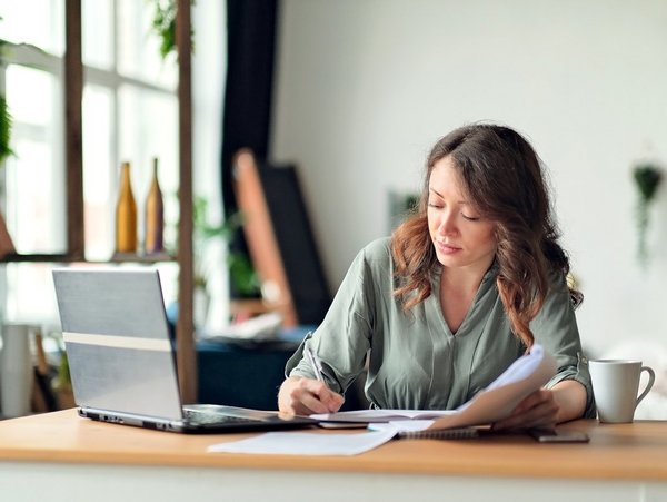 The image shows a woman working on documentation and using a laptop in an office setting