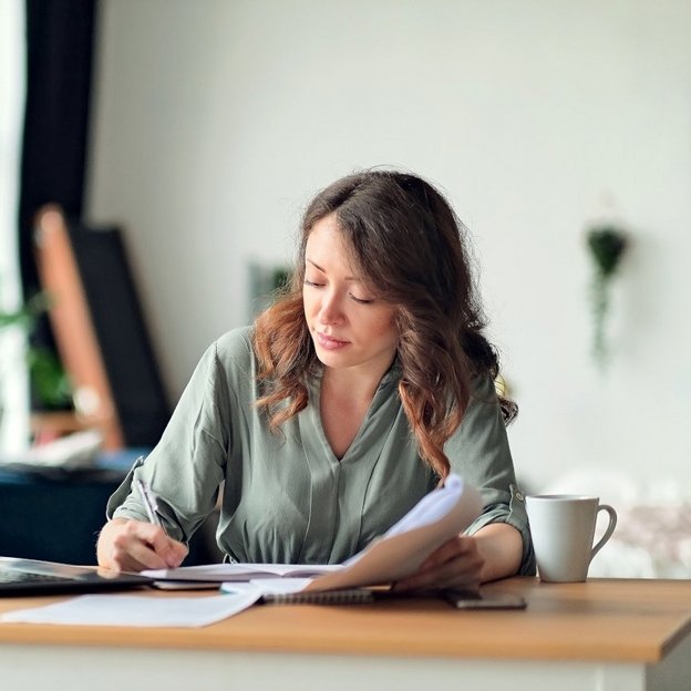 The image shows a woman working on documentation and using a laptop in an office setting