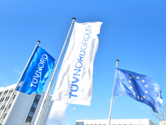 TÜV NORD and EU flags wave outside modern office buildings under a clear blue sky.