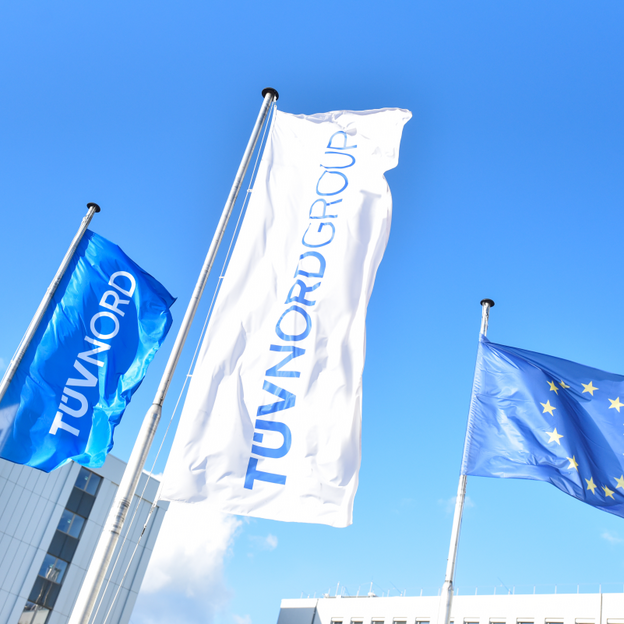 TÜV NORD and EU flags wave outside modern office buildings under a clear blue sky.