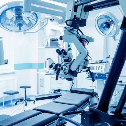Robotic surgery equipment set up in a modern operating room Robotic surgical system positioned over an operating table in a sterile operating room with medical equipment and overhead lights