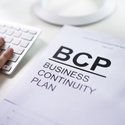 Business continuity plan document beside a computer keyboard Document labeled “BCP Business Continuity Plan” on a desk next to a keyboard and a hand using it