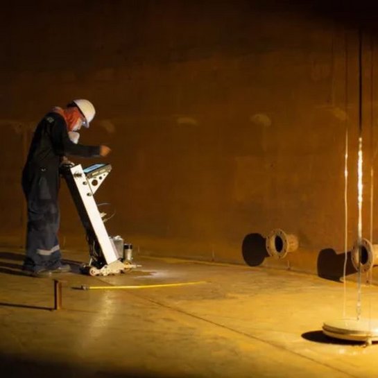 A worker in protective gear conducting an inspection inside a large industrial tank.