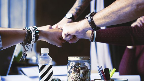 Teamwork and collaboration in action, as diverse hands unite in a powerful fist bump over a creative workspace.