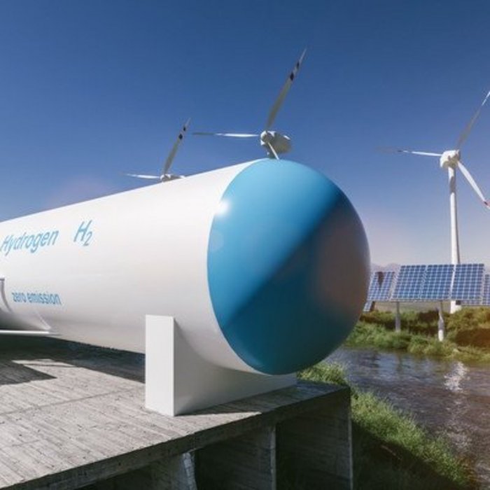 Wasserstofftank mit Aufschrift H₂ neben Windrädern und Solaranlagen zur nachhaltigen Energiegewinnung.