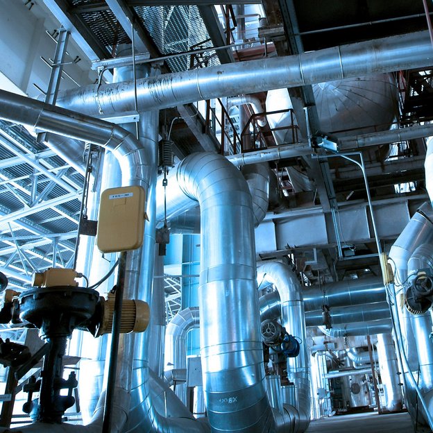 The picture is in a process industry. Metal pipes are going in diffrent directions, a blue light is shining of the pipes.