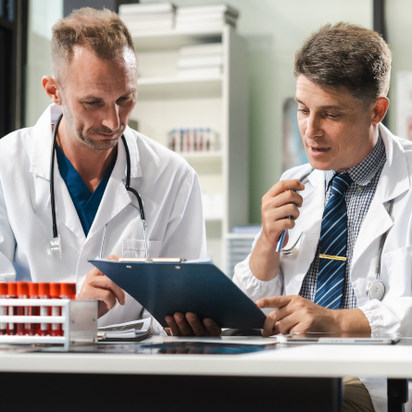 Två vårdpersonal, klädda i medicinska arbetskläder, granskar tillsammans en rapport Två vårdpersonal, klädda i medicinska arbetskläder, granskar tillsammans en rapport