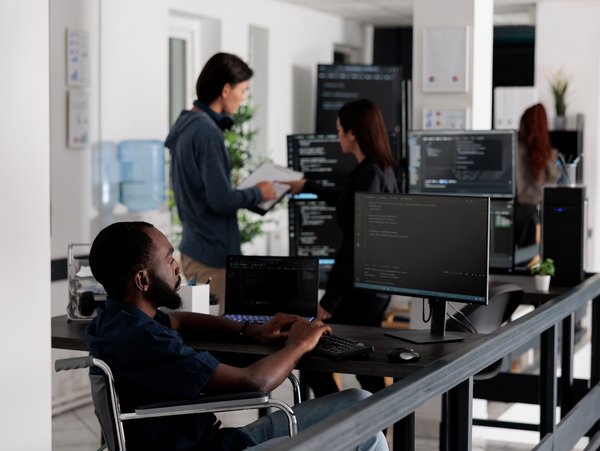 Modern office environment with personnel working on computers, discussing tasks, and collaborating on projects amidst a tech-focused setup.