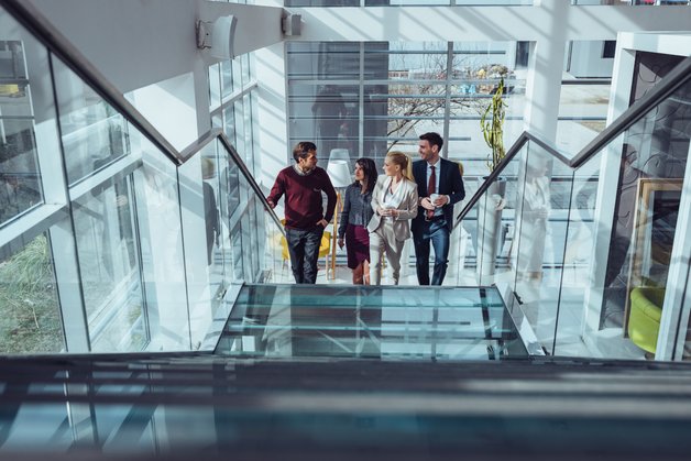The photo shows four people walking up the stairs and talking in a modern-looking building