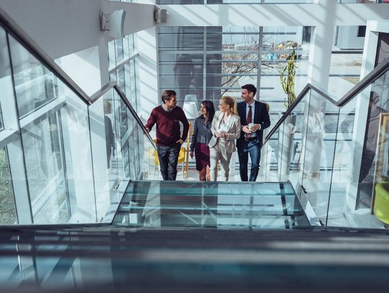 The photo shows four people walking up the stairs and talking in a modern-looking building