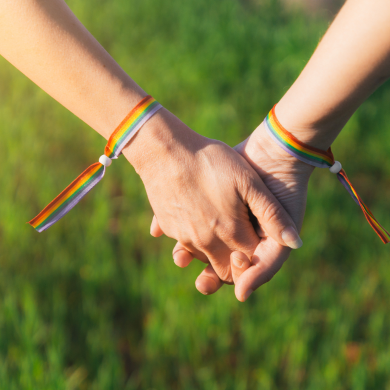 Two people are holding hands while wearing LGBTQIA+ pride bracelets