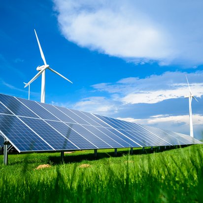 Solar and wind energy installation in a rural landscape Solar panels installed on a grassy field with wind turbines under a blue sky with scattered clouds.