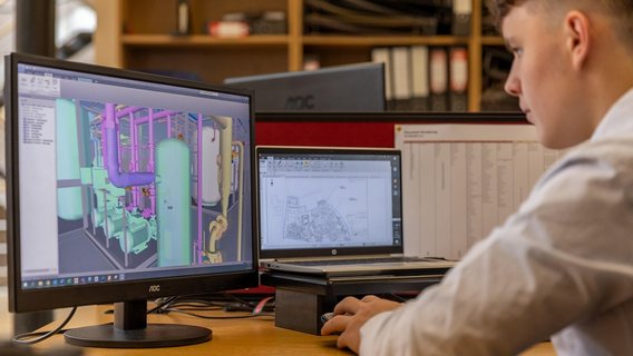  Engineering design and analysis in progress, featuring detailed 3D modeling and technical schematics on dual computer screens in a professional workspace.