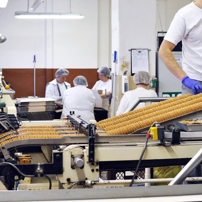 Industrial cookie production line with workers monitoring packaging and processing Workers wearing gloves overseeing a conveyor line of baked cookies in a food production facility, with additional staff and equipment in the background.