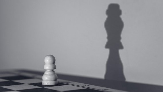 A chess pawn casts a queen's shadow, symbolizing potential, ambition, and possible transformation.