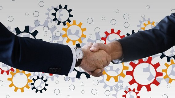 Two hands shake in front of interlocking gears, symbolizing partnership and collaborative success.