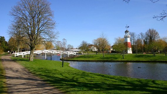 A scenic park in Kolding, Denmark, featuring a charming lighthouse and a quaint white bridge, ideal for relaxing nature walks.