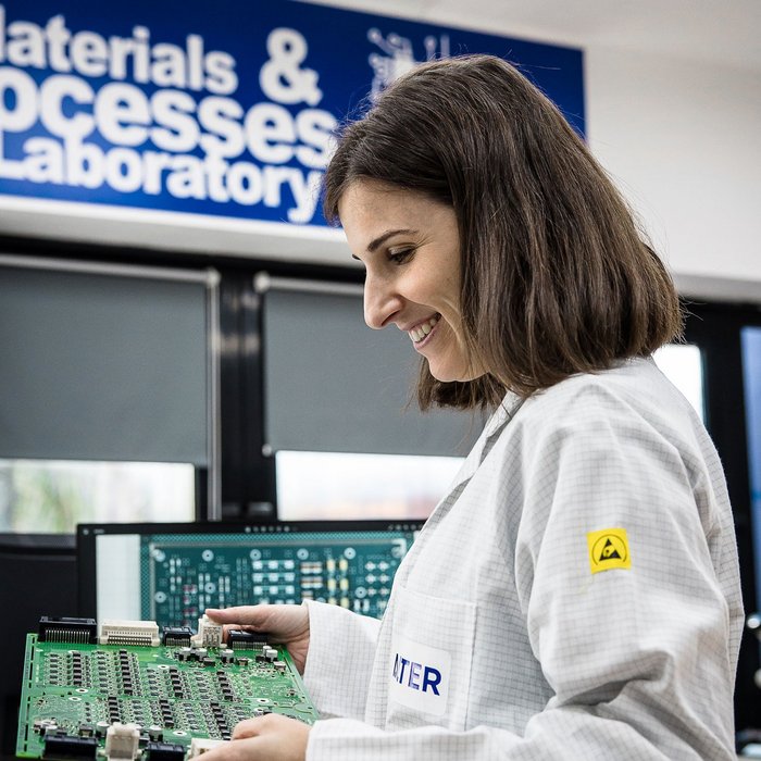 Eine Ingenieurin in einem weißen ESD-Schutzkittel untersucht eine Leiterplatte.