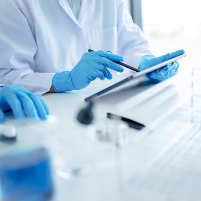 Two scientists wearing protective gloves are documenting data on a tablet Two scientists wearing protective gloves are documenting data on a tablet while working in a laboratory, possibly during an experiment or analysis.