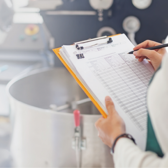 A person holding a clipboard with a checklist, standing next to industrial equipment.