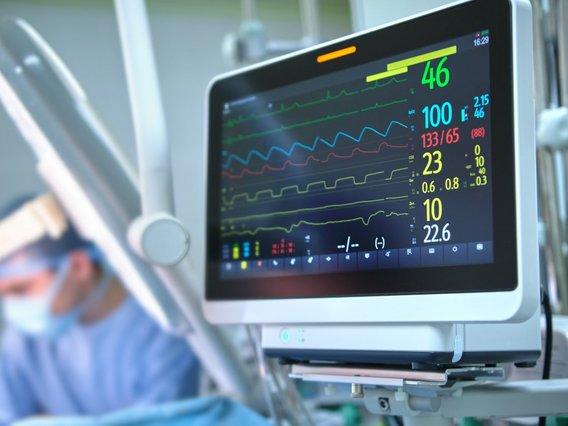 The image shows a heart rate and patient condition monitor in a hospital operating room during a surgical procedure