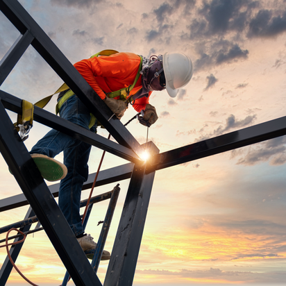 Construction worker welds steel beams at sunset, ensuring structural integrity. He has a hard hat and a safety harness. 